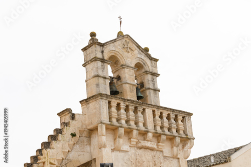 Old stone bell tower of a church with bells and a cross against the sky in southern Italy, Matera