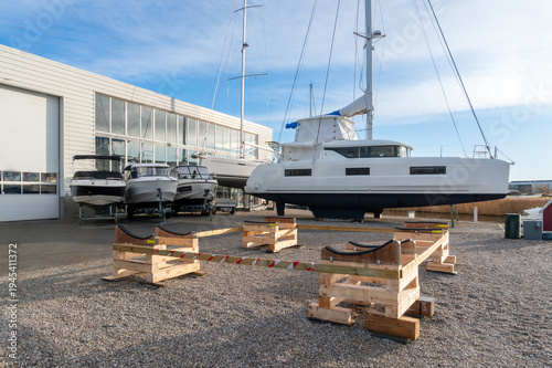 Obraz na plátne Ishoj Marina, Denmark – November 17, 2025: Sailing yacht lifted on wooden supports in a marina boatyard near a service hangar