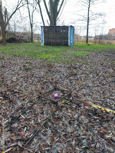 Colorful object placed in a muddy garden near a rustic shelter