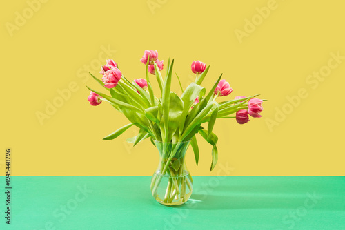 Bild auf Leinwand Bouquet of pink tulips in a glass vase on a green surface against a yellow backg