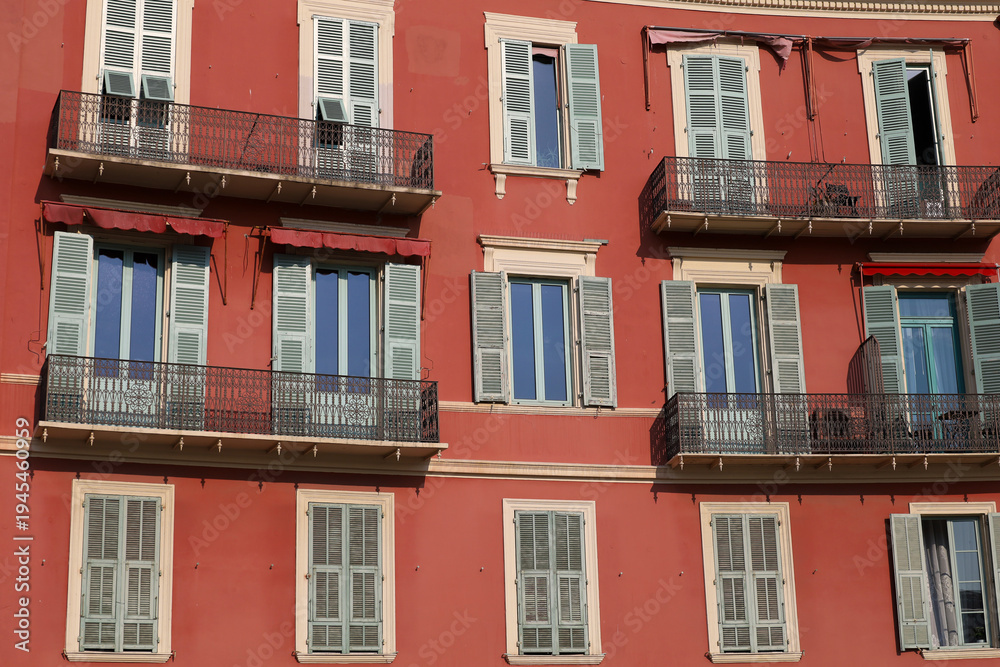 Obraz premium A classic Mediterranean-style building with red ochre walls, windows, and balconies with decorative wrought-iron railings. A typical façade of an old French residential building