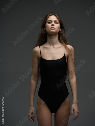 Young woman in black bodysuit posing confidently against dark background with serious expression and natural makeup