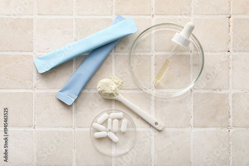 Collagen jelly sticks, pills, pipette and teaspoon of powder on beige tile background