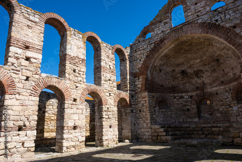 Canvastavla the Church of Saint Sophia ruins in Nesebar, Bulgaria, showcasing the rhythmic Byzantine arches and the central apse under a clear blue sky