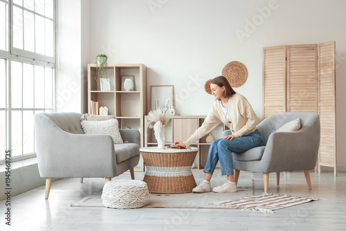 Beautiful young woman sitting on armchair with book in living room