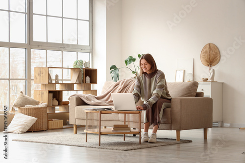 Beautiful young woman using modern laptop on sofa in living room