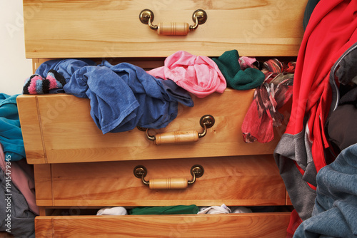 Dresser drawers filled with clothes in disarray, showing everyday clutter and unorganized personal items.