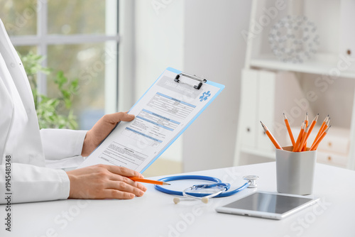 Female doctor with clipboard and tablet computer sitting at table in clinic, ...