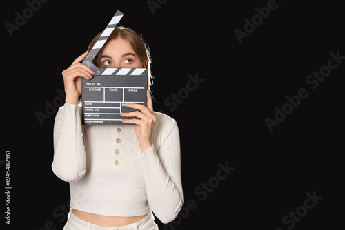 Foto Young actress with movie clapper on black background