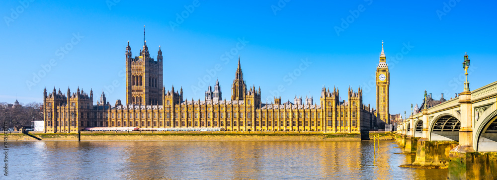 Fototapeta premium The Houses of Parliament and Big Ben along the River Thames. The sky is clear. People visit the area to admire this famous landmark.