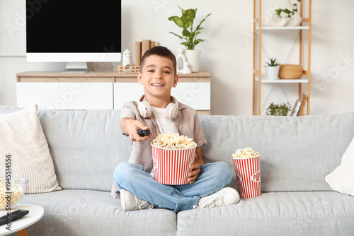 Cute happy boy with headphones, popcorn and TV remote control watching cartoo...
