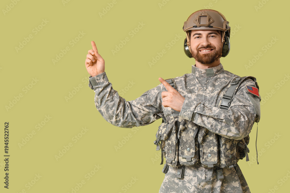 Obraz premium Young happy male soldier in uniform pointing at something on green background