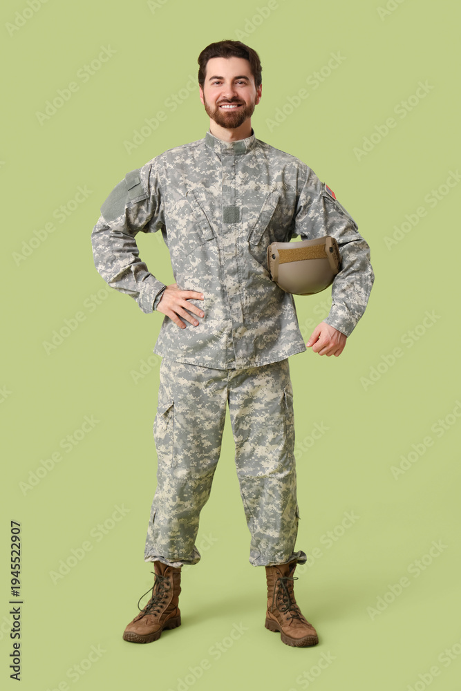 Fototapeta premium Young happy male soldier in uniform with helmet on green background