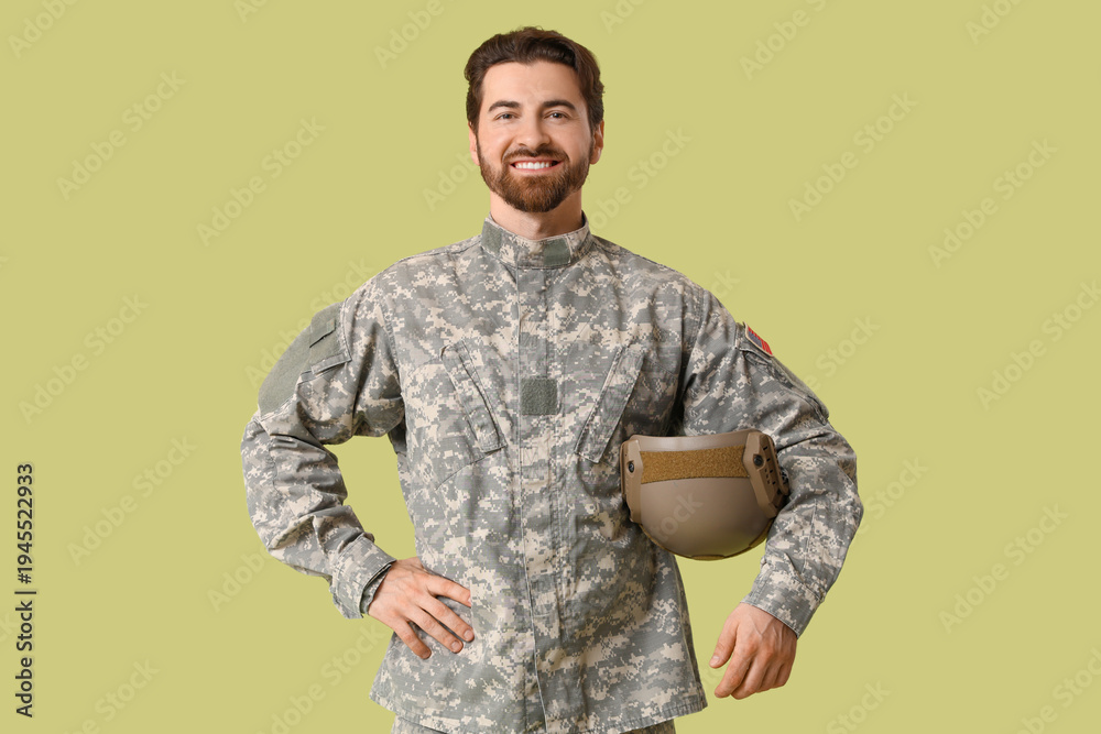 Obraz premium Young happy male soldier in uniform with helmet on green background