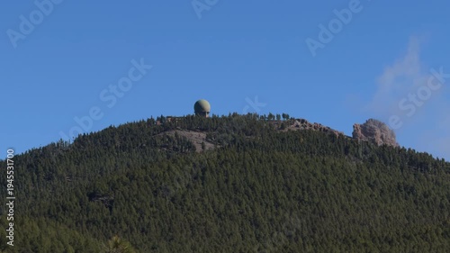 Static radar dome above forested mountain under clear sky
