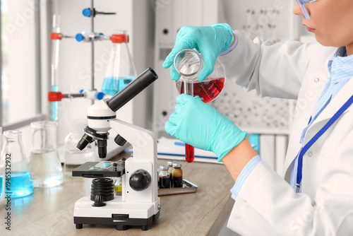 Female scientist pouring liquid from flask into test tube in laboratory, closeup