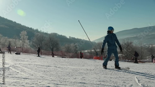 Snowboarder riding slowly on beginner ski slope with mountains and winter landscape