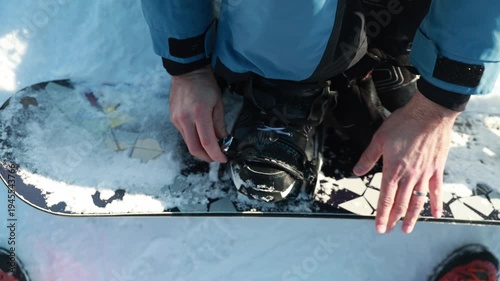 Snowboarder fastening snowboard binding on snowy slope preparing for ride