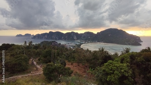 Golden sunset light illuminating tropical hills and coastline of Phi Phi Islands in southern Thailand. The dramatic sky and lush green forest create a peaceful travel atmosphere. The islands are known