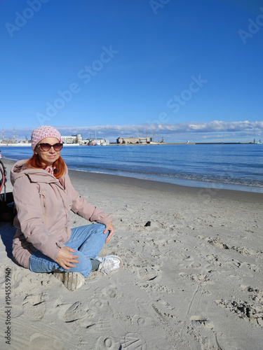 Young woman in autumn clothes practicing mindfulness on the beach under blue sky