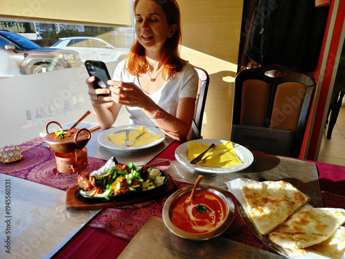 Smiling woman using smartphone while enjoying a colorful traditional indian dinner in restaurant