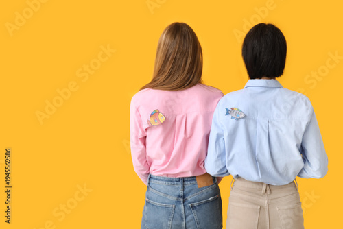 Beautiful young women with paper fishes attached to their backs on yellow bac...