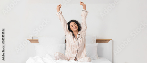 Young African-American woman stretching on bed in hotel room