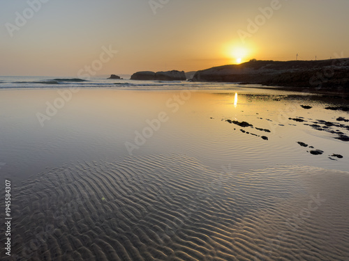 Ripples in wet sand reflecting sunrise light on empty Atlantic beach calm ocean morning minimal coastal landscape Cantabria Santander Virgen del Mar Spain