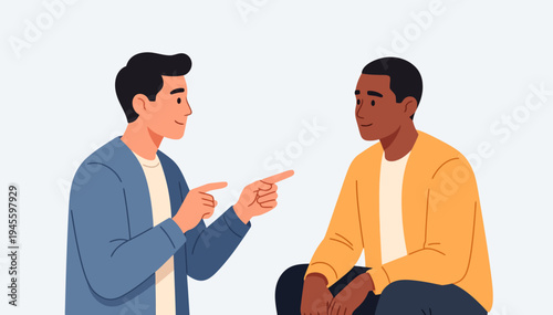 Two men engage in conversation. One points, gesturing with both hands. The other listens, smiling softly. Light background suggests casual, friendly interaction