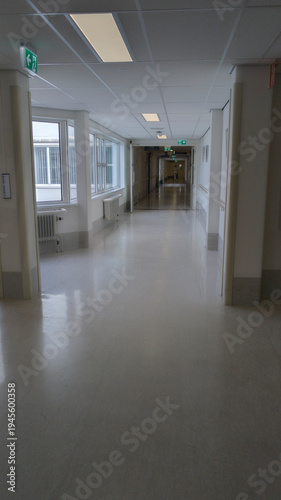 Empty Hospital Corridor With Natural Light, Clean Linoleum Floor and Illuminated Exit Signs