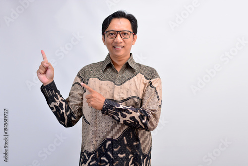 Professional Asian man in traditional batik pointing up and to the side for advertising copy space