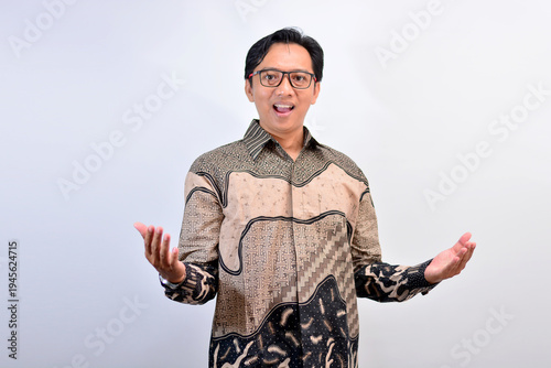 Friendly Southeast Asian man in batik shirt opening hands as if welcoming or presenting something