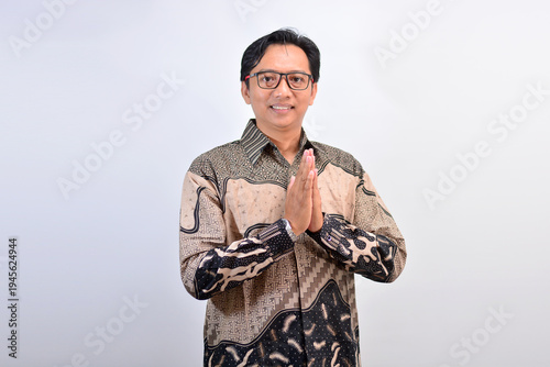 Friendly Southeast Asian man in batik shirt opening hands as if welcoming or presenting something