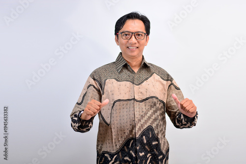 Cheerful Asian businessman in batik shirt pointing at himself with thumbs as a sign of confidence