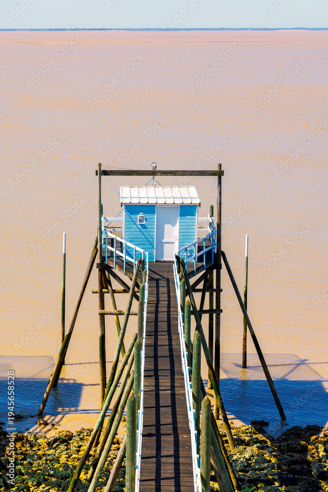 Fototapeta premium Fishing hut on stilts with wooden pier over calm estuary water