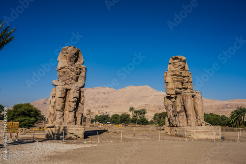Colossi of Memnon statues with desert mountains under clear blue sky