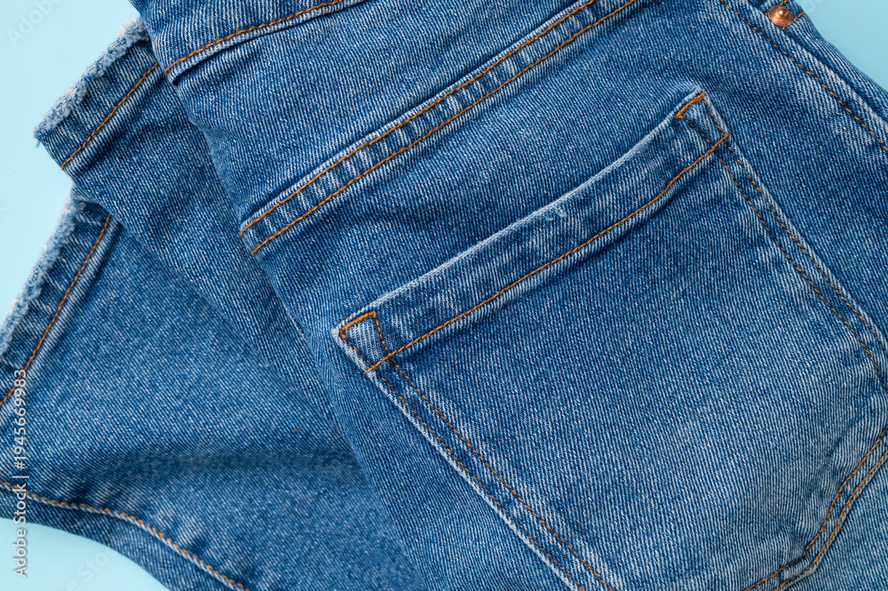 Fototapeta premium Blue jeans on light blue background flat lay top view. Denim, stylish casual pants, natural cotton fabric. Clothing concept, fashion, shopping, in-store sale, discounts