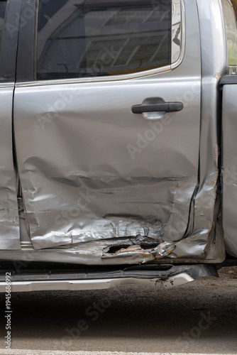 Severely damaged car door after a collision: the silver vehicle’s side panel shows extensive dents and tears, with exposed metal and broken paint revealing the impact’s force. 