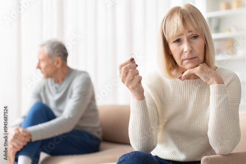 Obraz na płótnie Upset senior woman holding wedding ring while sitting apart from husband on sofa