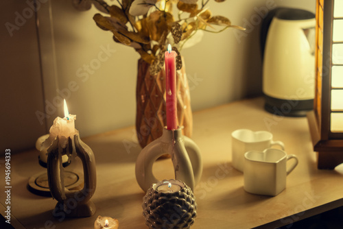 A cozy evening scene featuring a wooden table with glowing candles, a decorative vase with gold foliage, heart-shaped mugs, and an elegant Japanese-style wooden lamp, creating a warm atmosphere.