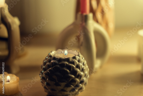 A single burning candle sits in a ceramic holder, creating a soft, warm glow. In the blurred background