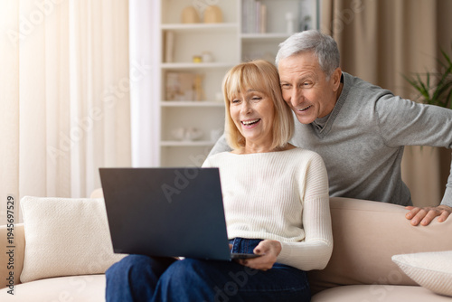Tableau sur toile Senior couple smiling while using laptop together at home