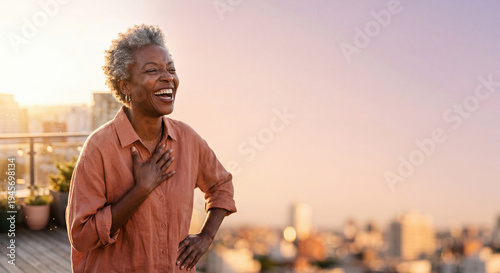 Radiant woman with silver hair laughing joyfully on rooftop terrace at golden hour with generous copy space