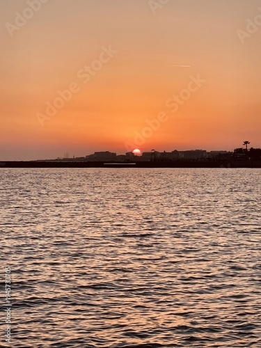 Low sun sinking behind coastal skyline over open water