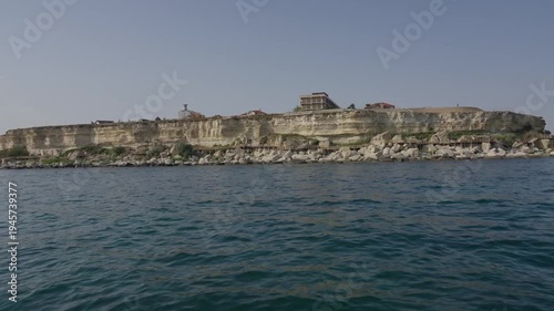 A worker in a blue apron handles a large sturgeon in an indoor fish farm tank.