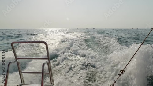 A powerful white wake trails behind a speeding motorboat on the open sea under a bright sun.