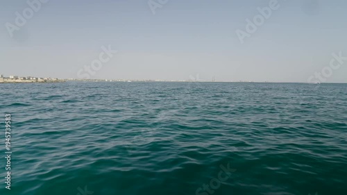 Calm deep blue ocean ripples under a clear sky with a distant coastal horizon during the day.