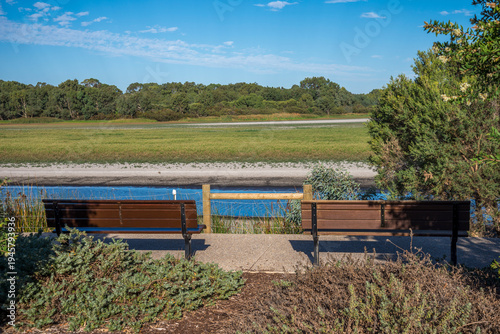 Two Park Benches Overlooking Riverbank and Marshland Landscape on a Sunny Day at Bibra Lake Reserve, 1 April 2021, Perth, Australia