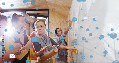 Designing team wearing casual attire placing sticky notes on whiteboard in studio with blue overlay
