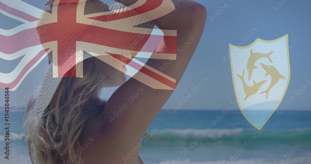 Fototapeta premium Adjusting sun hat, woman wearing swimsuit facing sea at beach, UnionJack overlay and dolphin emblem